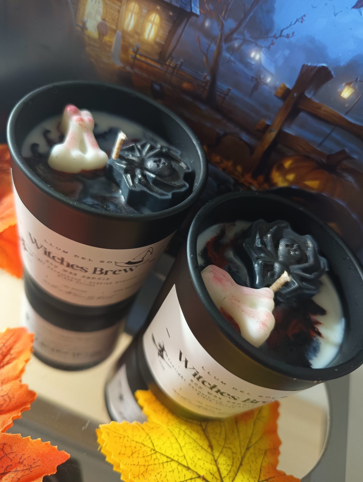 Two Halloween-themed candles with decorative elements on a table with autumn leaves.