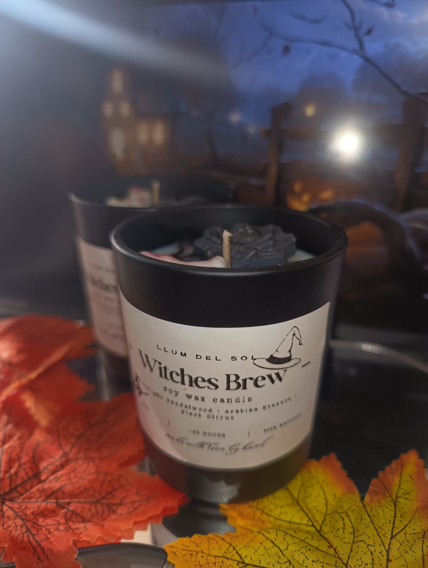 Candle labeled 'Witches Brew' with autumn leaves and a blurred background